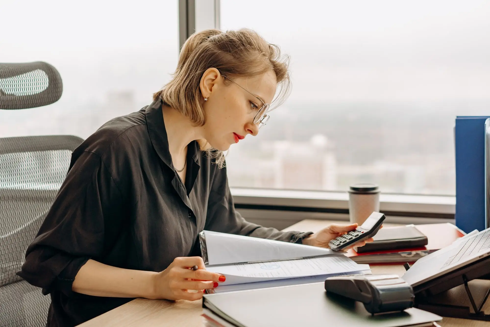Business owner checking an overdue customer account in a ring binder against a calculator before deciding whether to write the debt off